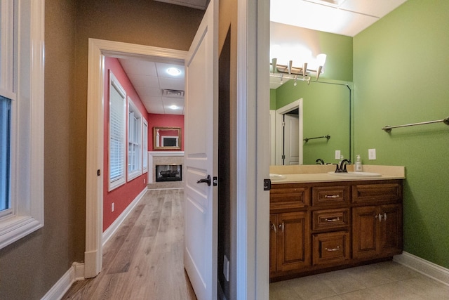 bathroom with a paneled ceiling, a fireplace, vanity, visible vents, and baseboards