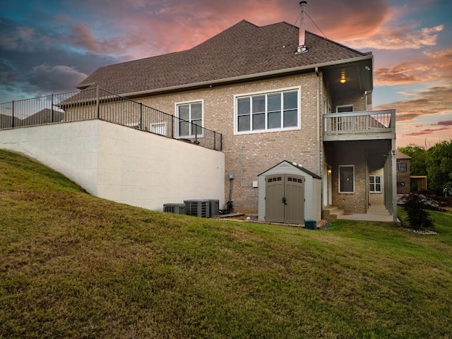 back of property at dusk featuring a yard, brick siding, an outdoor structure, and a storage unit