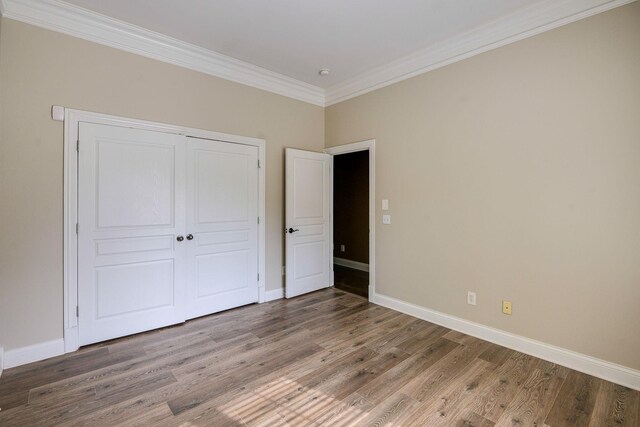 unfurnished bedroom featuring a closet, crown molding, baseboards, and wood finished floors