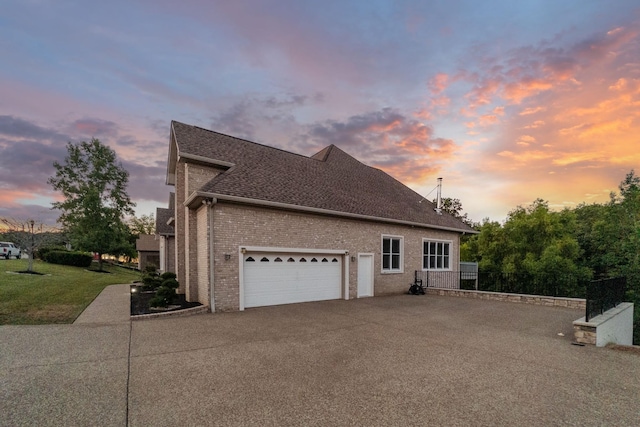 view of property exterior featuring a garage, brick siding, driveway, roof with shingles, and a lawn