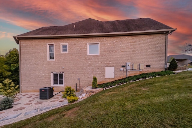 view of side of property with a yard, brick siding, a patio, and central air condition unit