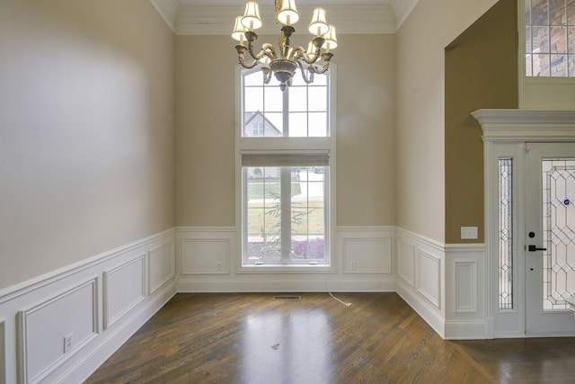 foyer entrance with dark wood-style floors, a wainscoted wall, ornamental molding, and an inviting chandelier