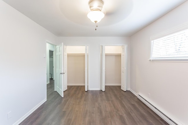 unfurnished bedroom with a baseboard radiator, dark wood-type flooring, a ceiling fan, baseboards, and two closets