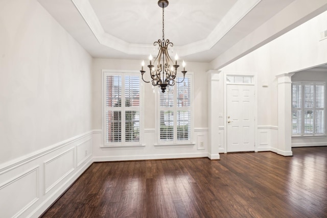 unfurnished dining area featuring wainscoting, ornamental molding, dark wood-type flooring, a tray ceiling, and a chandelier