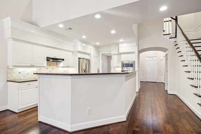 kitchen featuring under cabinet range hood, white cabinets, appliances with stainless steel finishes, decorative backsplash, and dark wood finished floors