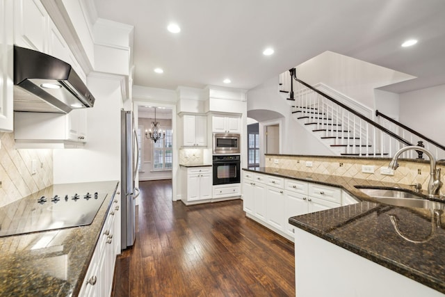 kitchen with a sink, white cabinetry, wall chimney range hood, dark stone counters, and black appliances