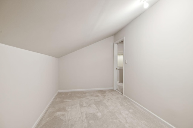 additional living space with light colored carpet, vaulted ceiling, and baseboards