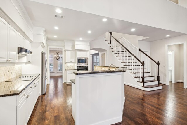 kitchen with black appliances, under cabinet range hood, white cabinetry, and dark stone counters