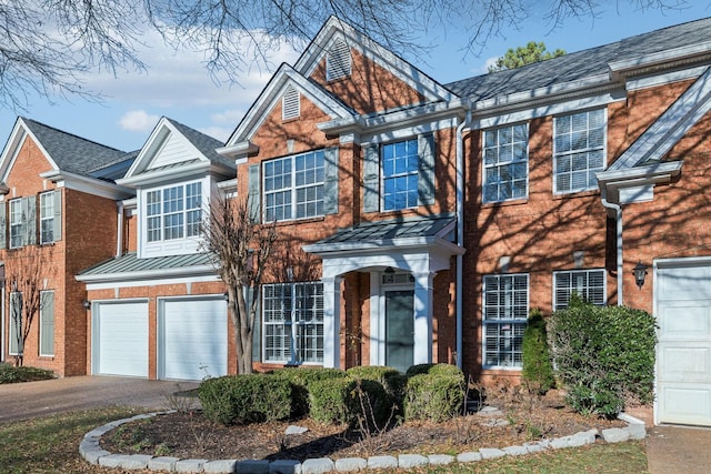 view of front facade featuring metal roof, a garage, brick siding, driveway, and a standing seam roof