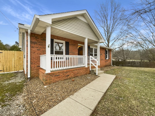 bungalow-style home with brick siding, a porch, fence, and a front yard