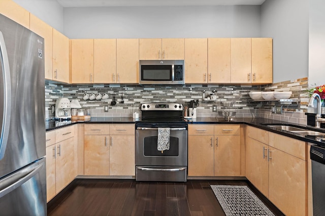 kitchen featuring light brown cabinetry, appliances with stainless steel finishes, dark countertops, and a sink