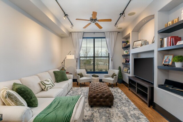 living room featuring track lighting, wood finished floors, a ceiling fan, and built in features