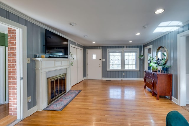 foyer entrance featuring light wood finished floors, recessed lighting, ornamental molding, a fireplace with flush hearth, and baseboards