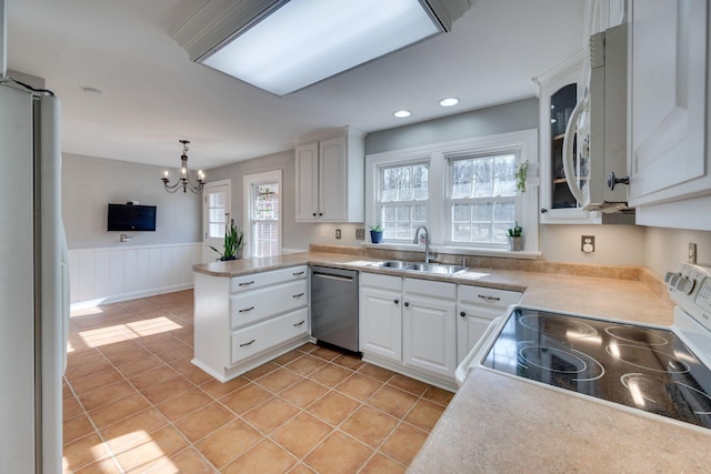 kitchen featuring a peninsula, white appliances, a sink, white cabinets, and wainscoting