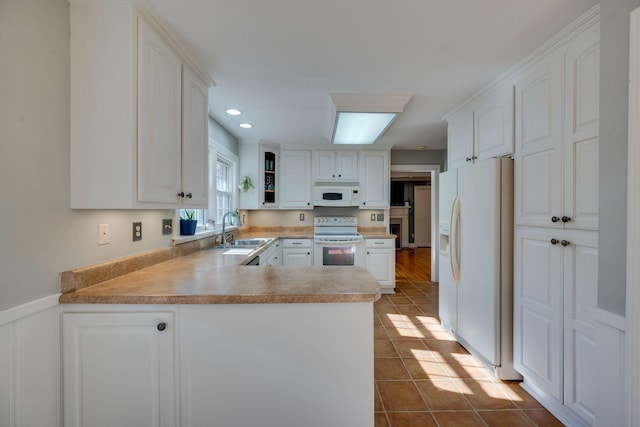 kitchen with white cabinets, a sink, tile patterned flooring, white appliances, and a peninsula