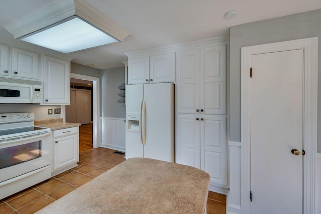 kitchen with white appliances, light tile patterned floors, a wainscoted wall, light countertops, and white cabinetry