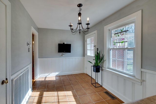 unfurnished dining area with wainscoting, visible vents, an inviting chandelier, and tile patterned floors