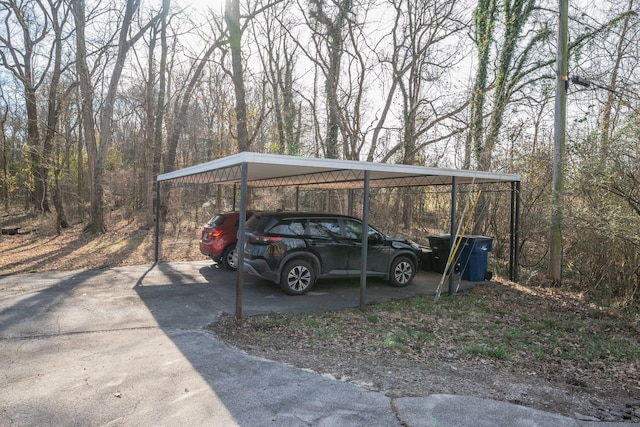 view of parking / parking lot featuring a wooded view, a carport, and concrete driveway