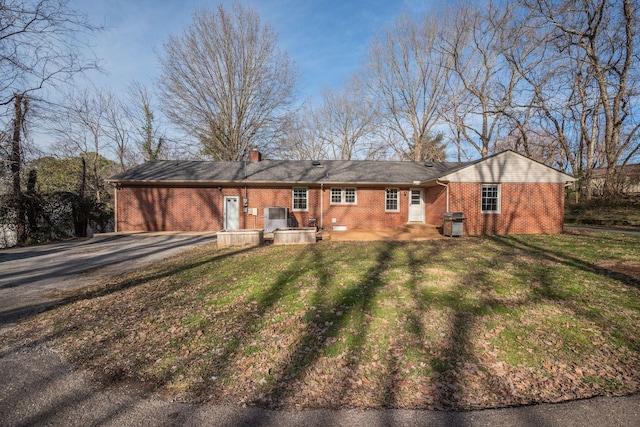 single story home with brick siding, driveway, a chimney, and a front lawn