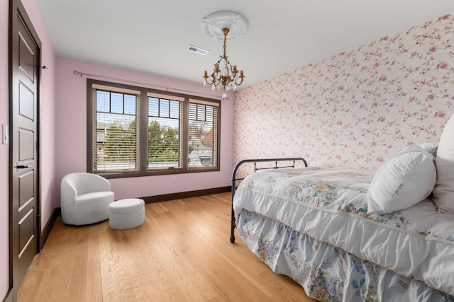 bedroom featuring visible vents, an inviting chandelier, light wood-type flooring, baseboards, and wallpapered walls