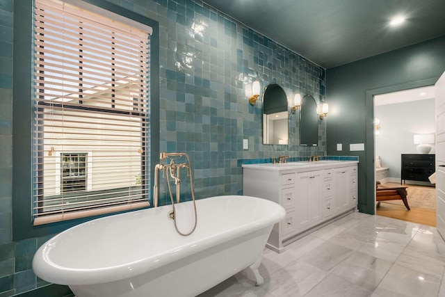 bathroom featuring a sink, tile walls, a freestanding bath, double vanity, and ensuite bath