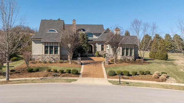 view of front facade featuring concrete driveway, a chimney, stone siding, and a front yard