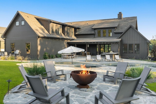 rear view of property featuring a fire pit, board and batten siding, a patio area, and an outdoor pool