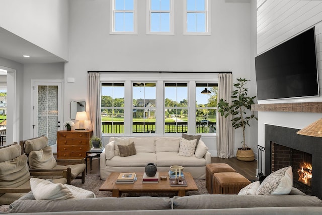 living area featuring a healthy amount of sunlight, a warm lit fireplace, a high ceiling, and wood finished floors