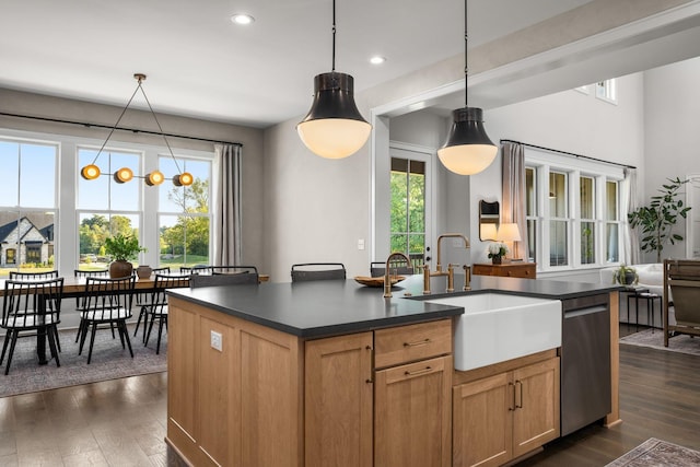 kitchen featuring dark countertops, decorative light fixtures, a sink, and an island with sink