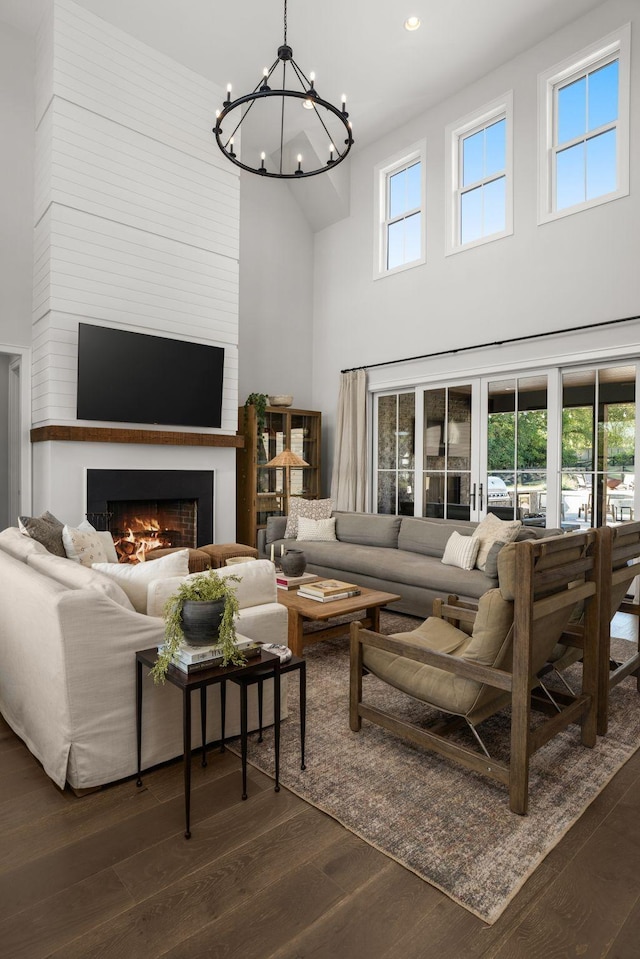 living room with a healthy amount of sunlight, dark wood-style floors, a warm lit fireplace, and a chandelier