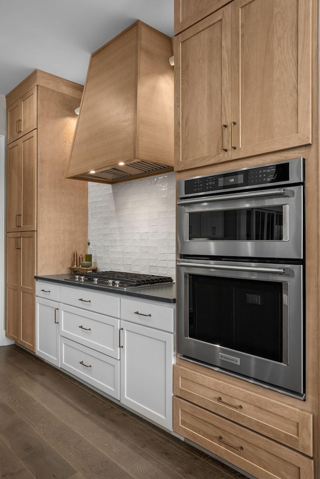 kitchen with white cabinets, dark countertops, dark wood-type flooring, stainless steel appliances, and premium range hood