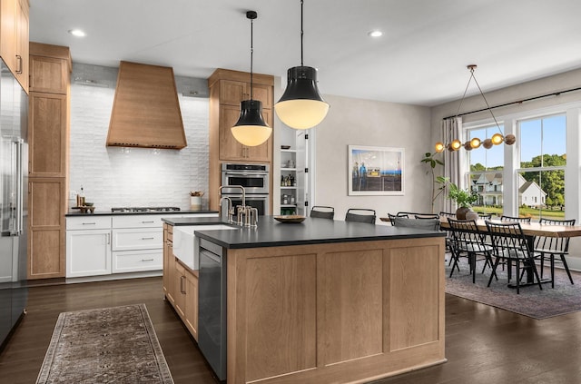 kitchen with pendant lighting, a center island with sink, dark countertops, white cabinetry, and premium range hood