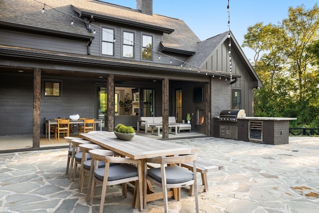 exterior space featuring a patio, outdoor dining area, an outdoor kitchen, a shingled roof, and a chimney