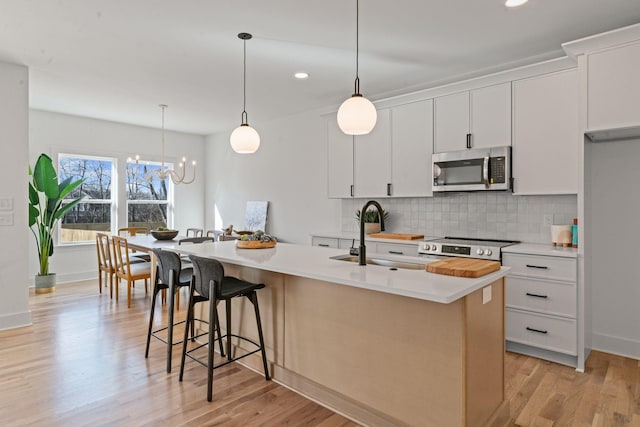 kitchen with an island with sink, stainless steel appliances, light countertops, white cabinetry, and a sink