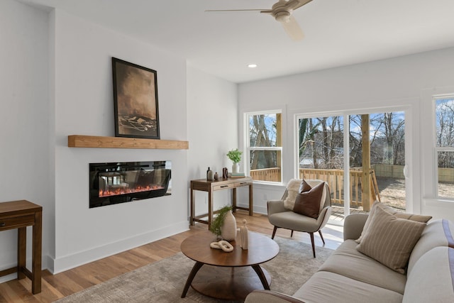 living area with baseboards, a glass covered fireplace, light wood-style flooring, and a healthy amount of sunlight