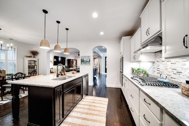 kitchen featuring arched walkways, a center island with sink, stainless steel appliances, open floor plan, and light stone countertops