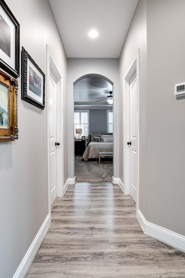 corridor featuring arched walkways, light wood-style flooring, and baseboards