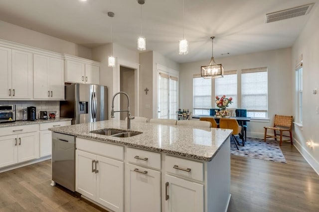 kitchen with a kitchen island with sink, stainless steel appliances, a sink, visible vents, and white cabinetry