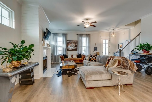 living room featuring light wood-type flooring, plenty of natural light, a fireplace, and stairway