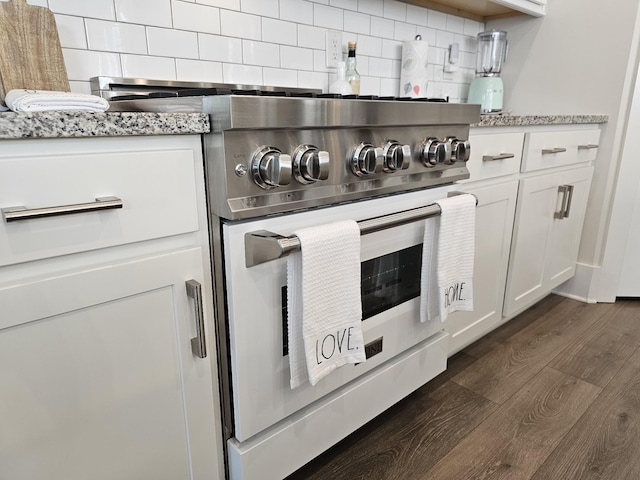 kitchen with light stone counters, dark wood-style floors, tasteful backsplash, high end stainless steel range oven, and white cabinetry