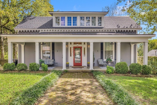 view of front of house featuring covered porch, a shingled roof, and a front yard