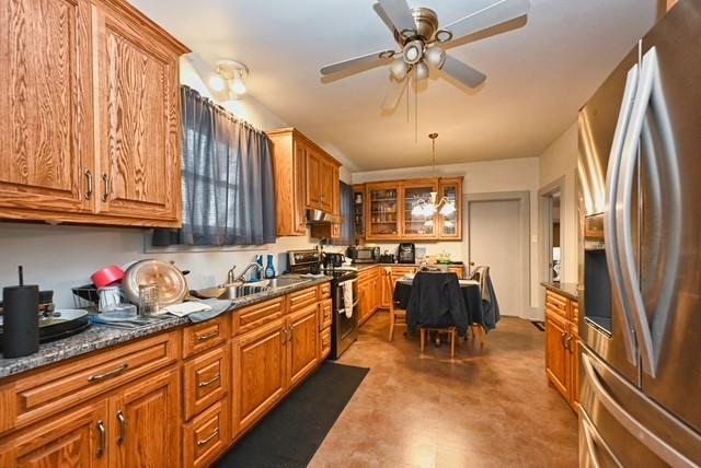 kitchen featuring stainless steel appliances, hanging light fixtures, brown cabinetry, glass insert cabinets, and dark stone counters