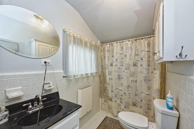 bathroom featuring toilet, a wainscoted wall, vaulted ceiling, vanity, and tile walls