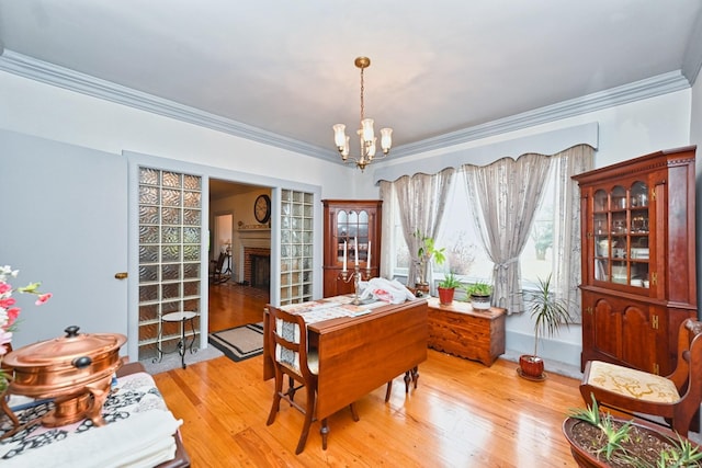 dining area with light wood-style floors, a chandelier, crown molding, and a fireplace