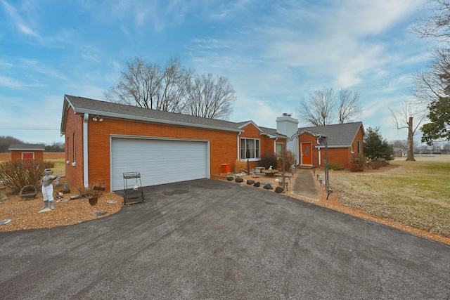 single story home featuring aphalt driveway, brick siding, a chimney, a front yard, and a garage