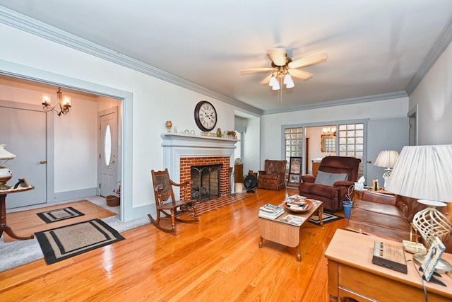 living room featuring crown molding, a brick fireplace, wood finished floors, baseboards, and ceiling fan with notable chandelier