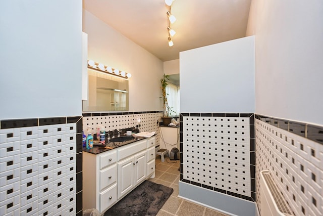 full bathroom with tile walls, rail lighting, a stall shower, vanity, and tile patterned flooring