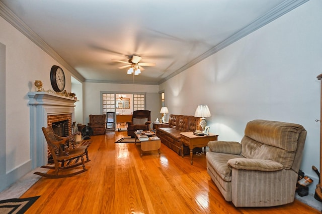 living area with ornamental molding, a brick fireplace, ceiling fan, and wood finished floors