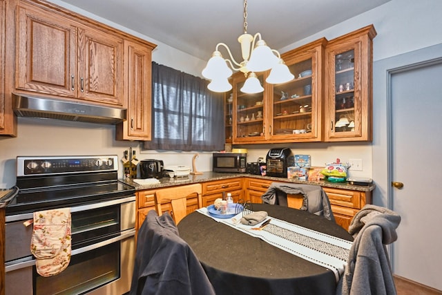 kitchen with under cabinet range hood, appliances with stainless steel finishes, brown cabinets, dark stone countertops, and glass insert cabinets