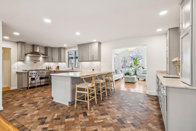 kitchen with range with two ovens, a breakfast bar area, tasteful backsplash, gray cabinets, and wall chimney exhaust hood